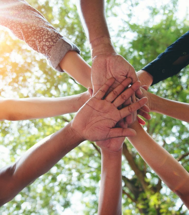 8 people each placing one outstretched hand on top of one another creating a start shape