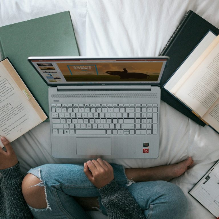 A person sat cross-legged in front of a laptop surrounded by books